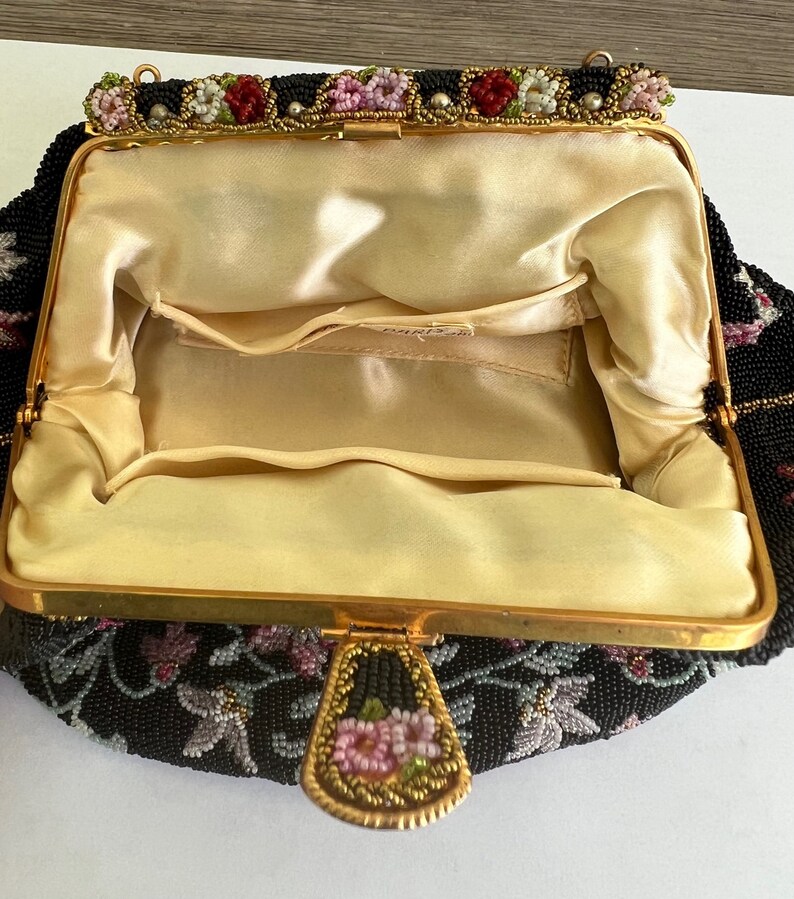 May include: A black beaded evening bag with a floral design and a gold clasp. The bag is lined with a cream-coloured fabric.