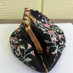May include: A black beaded evening bag with a floral design in pink, white, and green. The bag has a gold clasp and a beaded trim.