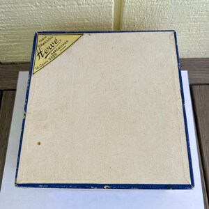 May include: A blue box with a white label that says "Herw&eacute;" in gold lettering. The label also says "Paris 12 Rue de la Paix Maroquinier Tel. Op&eacute;ra 2878".