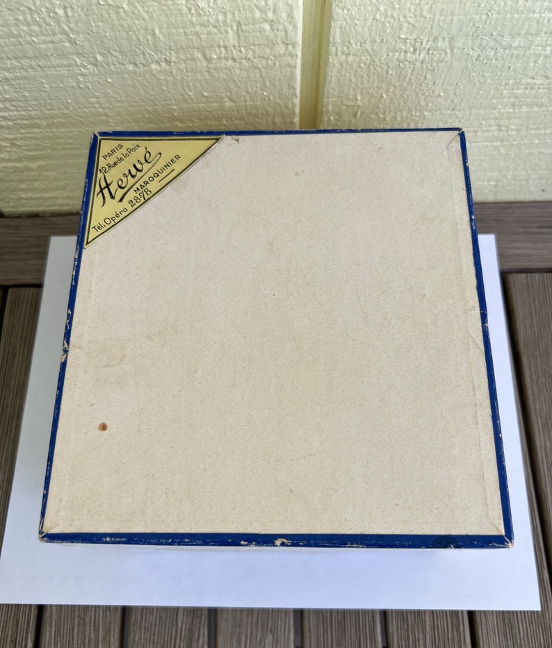 May include: A blue box with a white label that says "Herw&eacute;" in gold lettering. The label also says "Paris 12 Rue de la Paix Maroquinier Tel. Op&eacute;ra 2878".