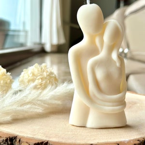 Peut inclure: Une sculpture de bougie blanche représentant un couple enlacé. La bougie est faite de cire blanche lisse et présente un design simple et moderne.