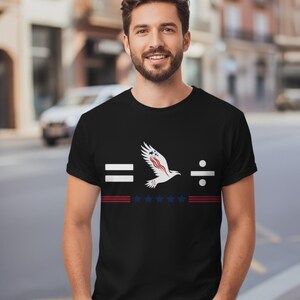 Peut inclure: T-shirt noir avec un motif graphique représentant un aigle, des étoiles et des rayures. Le motif comprend les symboles égal et division. L'aigle a des accents rouges, blancs et bleus.