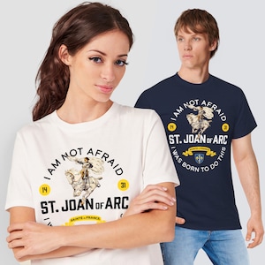 May include: Two white t-shirts with a navy blue t-shirt featuring a graphic of Joan of Arc on horseback with the text "I am not afraid" and "St. Joan of Arc" with a crest and the text "I was born to do this".