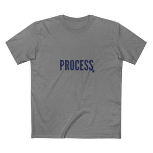 May include: A gray t-shirt with the word "PROCESS" printed in navy blue across the chest. A small navy blue star is next to the word. The shirt has short sleeves and a crew neck.