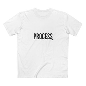May include: White t-shirt with the word "PROCESS" printed in black, accompanied by a small black star. The shirt has short sleeves and a crew neck.