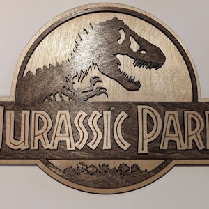 Op de afbeelding: Een houten bord met het Jurassic Park logo. Het logo toont een dinosaurus silhouet en de tekst "Jurassic Park" in een gestileerd lettertype.