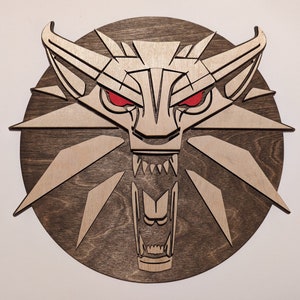 May include: A wooden wall decor featuring a stylized wolf head with red eyes and a snarling mouth. The wolf head is surrounded by a circular wooden frame.