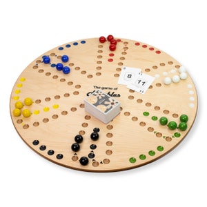 May include: A wooden board game with a circular design. The board features holes and colored marbles in red, blue, yellow, green, white, and black. A deck of cards and two numbered cards are also on the board. The game is called "Doublebles".