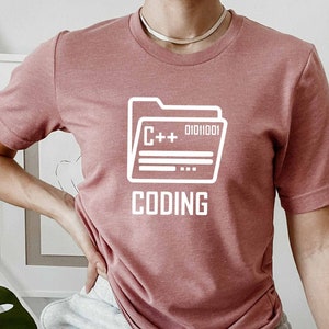 May include: A pink t-shirt with a white graphic of a folder labeled "C++" and "Coding".