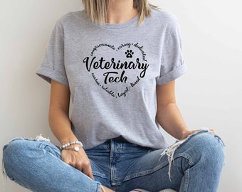 May include: A gray t-shirt with a black circle design that says "Veterinary Tech" with a paw print and the words "compassionate, caring, dedicated, warm, reliable, loyal, kind" around the circle.
