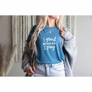 May include: A teal blue t-shirt with the text "I grind but most of all I pray" in white lettering.
