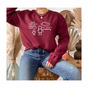 K&ouml;nnte beinhalten: Burgunderfarbener Pullover mit einem wei&szlig;en Aufdruck, der "Papa, woraus bestehen Wolken? Linux-Server, meistens." Der Aufdruck enth&auml;lt auch eine Strichm&auml;nnchenzeichnung eines Elternteils und eines Kindes.