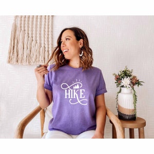 May include: A purple t-shirt with the word "HIKE" in white lettering with a stylized font and a graphic of trees and a sun above the word.