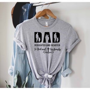 May include: Gray t-shirt with a black graphic that says "DAD DEDICATED AND DEVOTED TO God and his family" with a silhouette of a father and children.