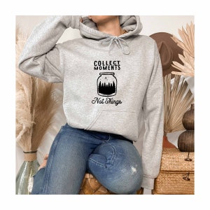 May include: Gray hooded sweatshirt with a black graphic of a jar with trees inside and the text "Collect Moments Not Things".