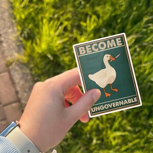 May include: A sticker featuring a white goose holding a knife, with the words "BECOME UNGOVERNABLE" in a rectangular frame. The background is teal, and the goose has orange feet and beak.