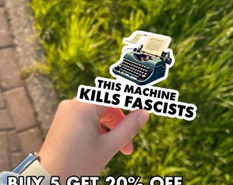 May include: A sticker featuring a teal typewriter with the text "THIS MACHINE KILLS FASCISTS" in bold, black letters. The sticker is held against a background of green grass. The image also includes the text "BUY 5 GET 20% OFF".