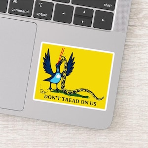 May include: A yellow sticker featuring a blue bird with outstretched wings, a snake, and the text "DON'T TREAD ON US." The bird has a white star on its chest and is holding the snake. The snake is yellow and black.