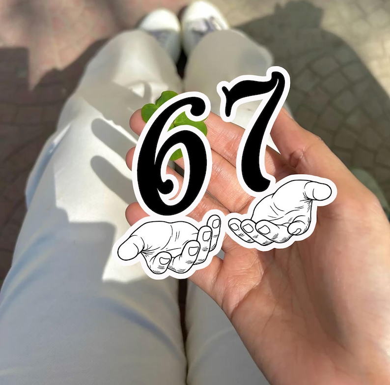May include: A hand holding a green leaf with the numbers "67" in black. Below the numbers are two illustrations of hands with open palms. The person is wearing white pants and white shoes.