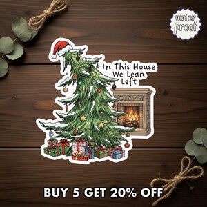 May include: A waterproof sticker featuring a Christmas tree with a Santa hat, ornaments, and the text "In This House We Lean Left." A fireplace and wrapped gifts are also shown. The sticker is designed for holiday decor.