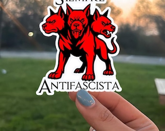 May include: A sticker featuring a three-headed red dog with the words "SIEMPRE ANTIFASCISTA" in white. The sticker is held by a hand with blue nail polish. The text "BUY 5 GET 20% OFF" is at the bottom.