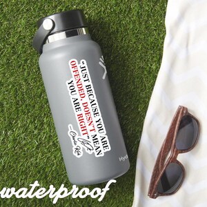 May include: A gray water bottle with a black lid and a white sticker that reads "JUST BECAUSE YOU ARE OFFENDED, DOESN'T MEAN YOU ARE RIGHT" by Charlie Kirk. The word "waterproof" is at the bottom. Brown sunglasses are next to the bottle.