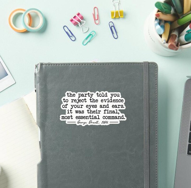 May include: A gray notebook with the quote "the party told you to reject the evidence of your eyes and ears. It was their final, most essential command. George Orwell, 1984." Colorful office supplies surround the notebook.