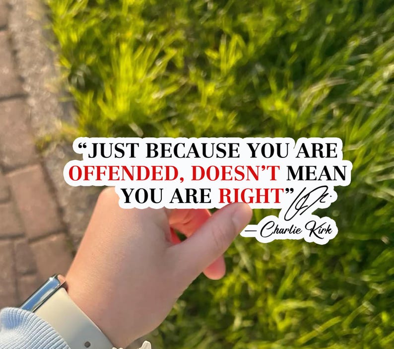 May include: A white sticker with the quote "JUST BECAUSE YOU ARE OFFENDED, DOESN'T MEAN YOU ARE RIGHT" by Charlie Kirk. The sticker is held in front of a background of green grass and a brick walkway.