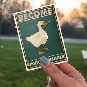 May include: A sticker with a cartoon goose holding a knife. The sticker has the words "BECOME UNGOVERNABLE" in a vintage style font. The goose is white with orange feet and beak, set against a teal background.