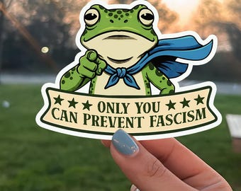 May include: A sticker featuring a cartoon frog in a superhero cape, pointing at the viewer. The sticker has the text "ONLY YOU CAN PREVENT FASCISM" on a banner. The frog is green with black spots.