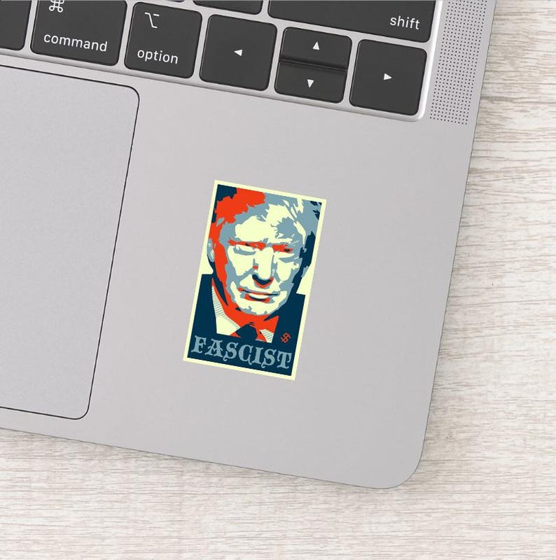 May include: A sticker featuring a stylized portrait with red, blue, and yellow tones. The word "FASCIST" is printed in a blue box at the bottom. The sticker is placed on a laptop.