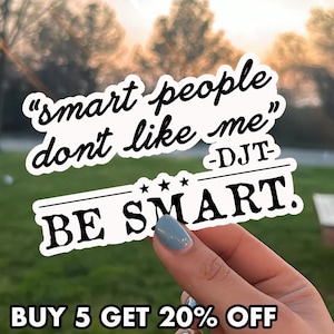 May include: A white sticker with black text that reads "smart people don't like me" and "BE SMART." The sticker is held by a hand with a blue painted nail. The text "BUY 5 GET 20% OFF" is at the bottom.