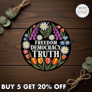 May include: A round, black sticker with the words "FREEDOM DEMOCRACY TRUTH" in white, surrounded by colorful flowers. The sticker has a "water proof" label. The phrase "BUY 5 GET 20% OFF" is at the bottom.