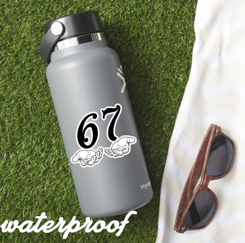 May include: A gray water bottle with a black lid and a white sticker featuring the number 67 and two hands. The word "waterproof" is at the bottom. Brown sunglasses rest on a white towel on a green surface.