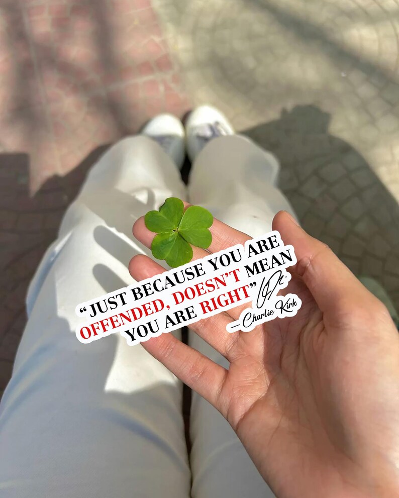 May include: A hand holding a four-leaf clover with a sticker that reads "JUST BECAUSE YOU ARE OFFENDED, DOESN'T MEAN YOU ARE RIGHT" by Charlie Kirk. The clover is bright green.
