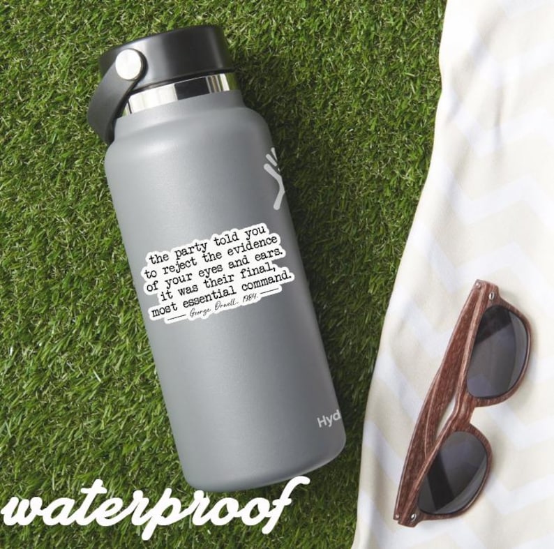 May include: A gray insulated water bottle with a black lid and a white sticker featuring a quote from George Orwell's "1984." The sticker reads, "the party told you to reject the evidence of your eyes and ears..." Wooden-framed sunglasses rest on a white cloth.