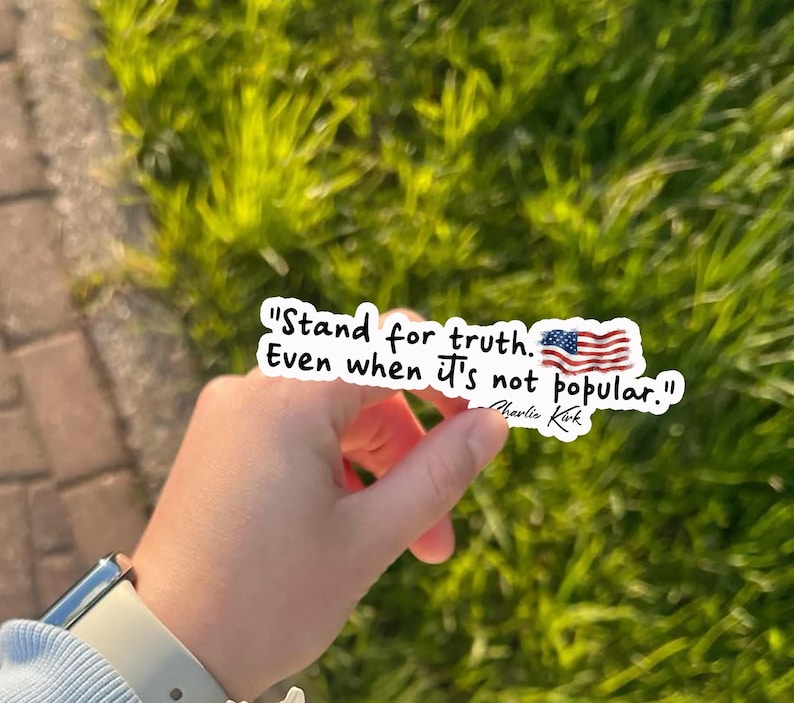 May include: A white sticker with the text "Stand for truth. Even when it's not popular." and an American flag graphic. The sticker is held against a background of green grass and a brick walkway.
