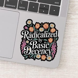 May include: A sticker with the text "Radicalized by Basic Decency" in a black and white design. The text is surrounded by a floral border of orange tulips, white daisies, and purple flowers.