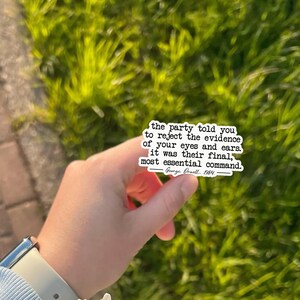 May include: A white sticker with black text quoting George Orwell: "the party told you to reject the evidence of your eyes and ears. it was their final, most essential command." The sticker is held against a green background.