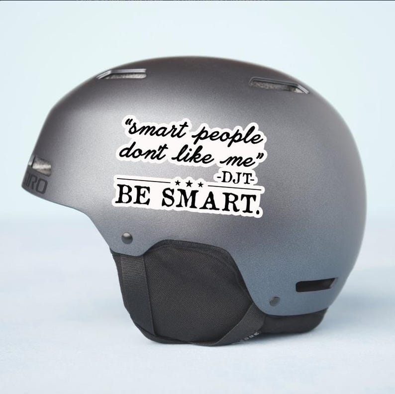 May include: A gray ski helmet with the text "smart people don't like me - DJT - BE SMART" in black and white. The helmet has a black chin strap and the Giro logo.