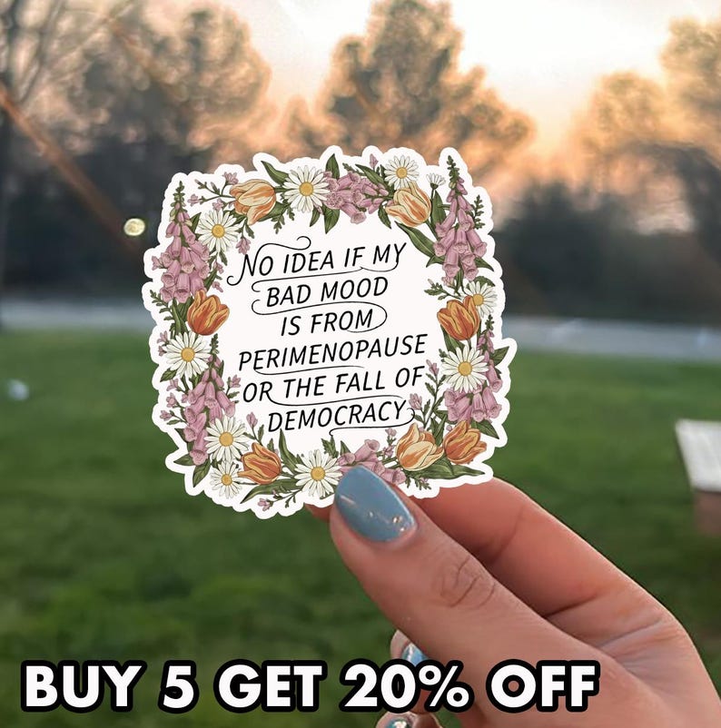 May include: A white sticker with a floral border featuring the text: "NO IDEA IF MY BAD MOOD IS FROM PERIMENOPAUSE OR THE FALL OF DEMOCRACY." The sticker is decorated with orange tulips, white daisies, and purple flowers.