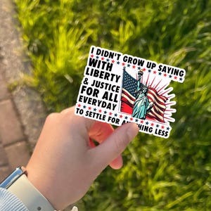 Peut inclure: Un autocollant repr&eacute;sentant la Statue de la Libert&eacute; et le drapeau am&eacute;ricain. L'autocollant porte le texte "I didn't grow up saying with liberty & justice for all everyday to settle for anything less."