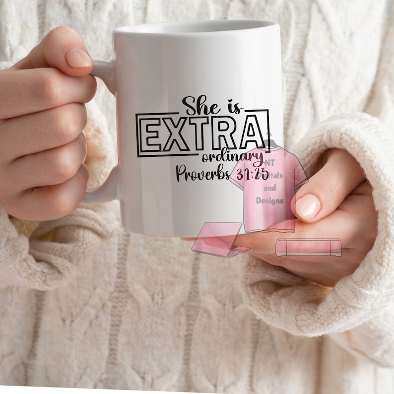 May include: White ceramic mug with the text "She is EXTRA ordinary Proverbs 31:25" in black. The mug is held by a person wearing a cream-colored sweater. The mug has a handle on the right side.