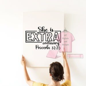 May include: A white canvas with the words "She is EXTRA ordinary Proverbs 31:25" in black script. A person is holding the canvas. A pink t-shirt design and a pink laptop are also visible.