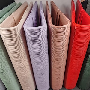 May include: A collection of eight leather-bound journals in various colors, including light blue, green, beige, lavender, pink, red, dark green, and black.