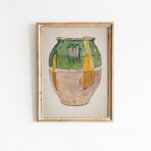 May include: A framed watercolor painting of a green and brown ceramic jar with a handle. The jar is painted in a rustic style with shades of green, brown, and yellow.