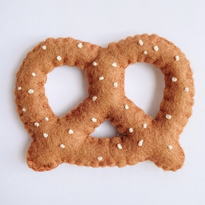 May include: A brown felt pretzel with white stitching, resembling a traditional pretzel.