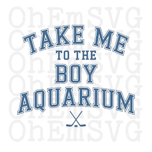 May include: A white graphic with blue text that reads "TAKE ME TO THE BOY AQUARIUM." Below the text are two crossed hockey sticks. The text has a collegiate style font.