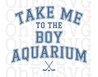 May include: A white graphic with blue text that reads "TAKE ME TO THE BOY AQUARIUM." Below the text are two crossed hockey sticks. The text has a collegiate style font.