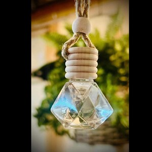 May include: A clear glass diamond-shaped car air freshener with a wooden cap and a natural fiber string.